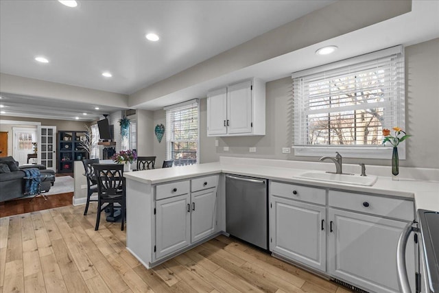 kitchen with appliances with stainless steel finishes, sink, white cabinets, kitchen peninsula, and light hardwood / wood-style flooring