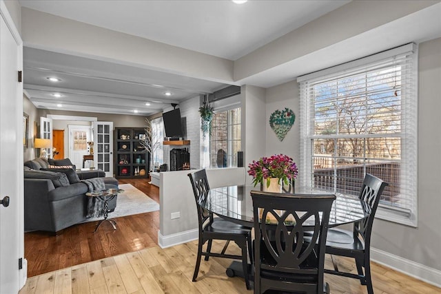 dining space with beam ceiling, a brick fireplace, a wealth of natural light, and light wood-type flooring