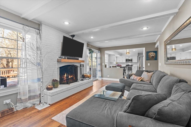 living room with a brick fireplace, beam ceiling, ornamental molding, and hardwood / wood-style flooring