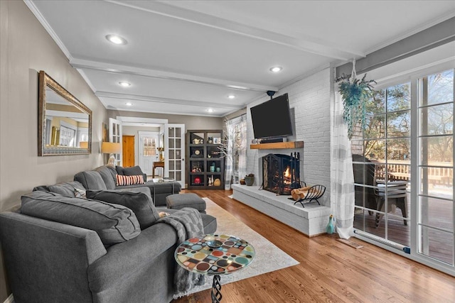 living room with beamed ceiling, wood-type flooring, crown molding, and a brick fireplace