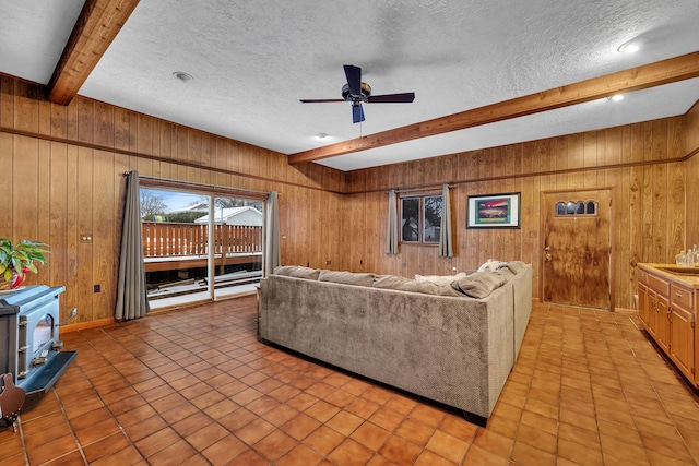 living room featuring light tile patterned flooring, wooden walls, beamed ceiling, ceiling fan, and a textured ceiling