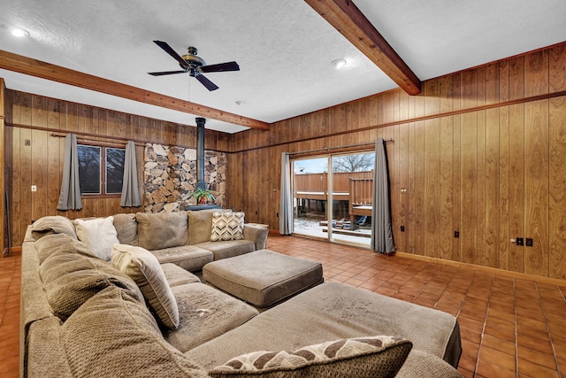 living room with wood walls, a textured ceiling, a wood stove, beam ceiling, and tile patterned flooring