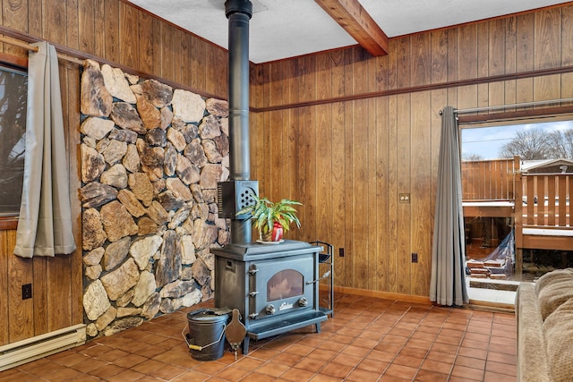 living room featuring light tile patterned floors, wooden walls, a baseboard radiator, beamed ceiling, and a wood stove