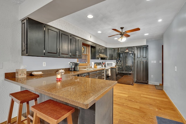 kitchen featuring black fridge with ice dispenser, sink, a breakfast bar area, kitchen peninsula, and stainless steel electric stove