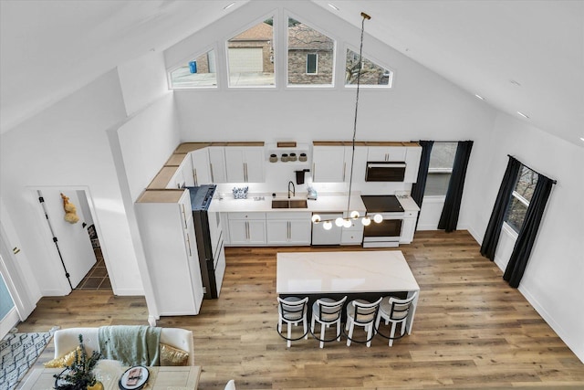 kitchen with high vaulted ceiling, white cabinets, hanging light fixtures, and range