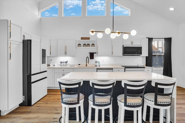 kitchen featuring refrigerator, sink, a center island, white cabinetry, and decorative light fixtures