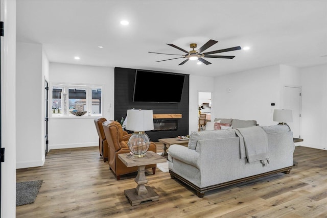 living room featuring ceiling fan, a large fireplace, and hardwood / wood-style floors