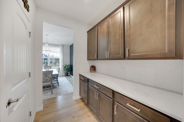 interior space with pendant lighting, decorative backsplash, dark brown cabinetry, light stone counters, and light hardwood / wood-style floors