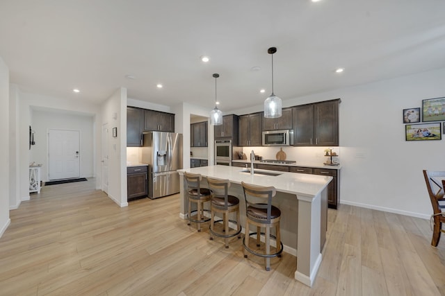 kitchen featuring dark brown cabinetry, decorative light fixtures, a center island with sink, and appliances with stainless steel finishes