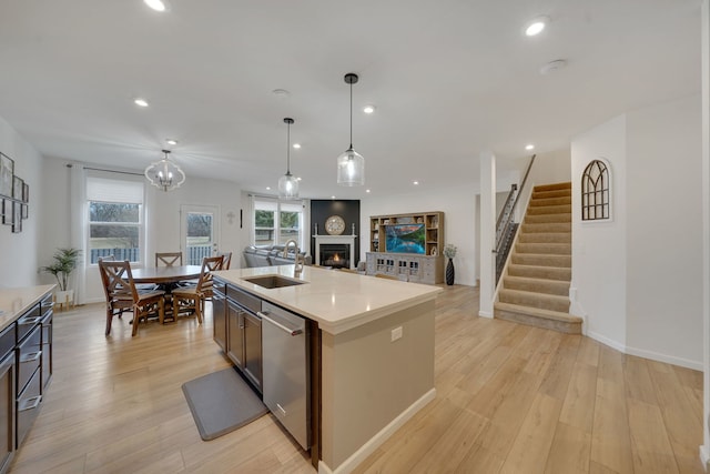 kitchen with sink, decorative light fixtures, light hardwood / wood-style flooring, dishwasher, and a kitchen island with sink