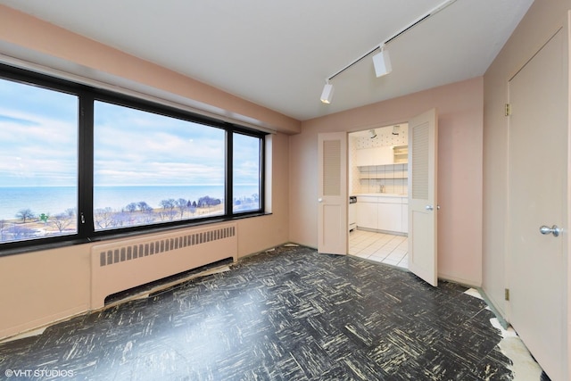 unfurnished room featuring radiator, track lighting, and a water view