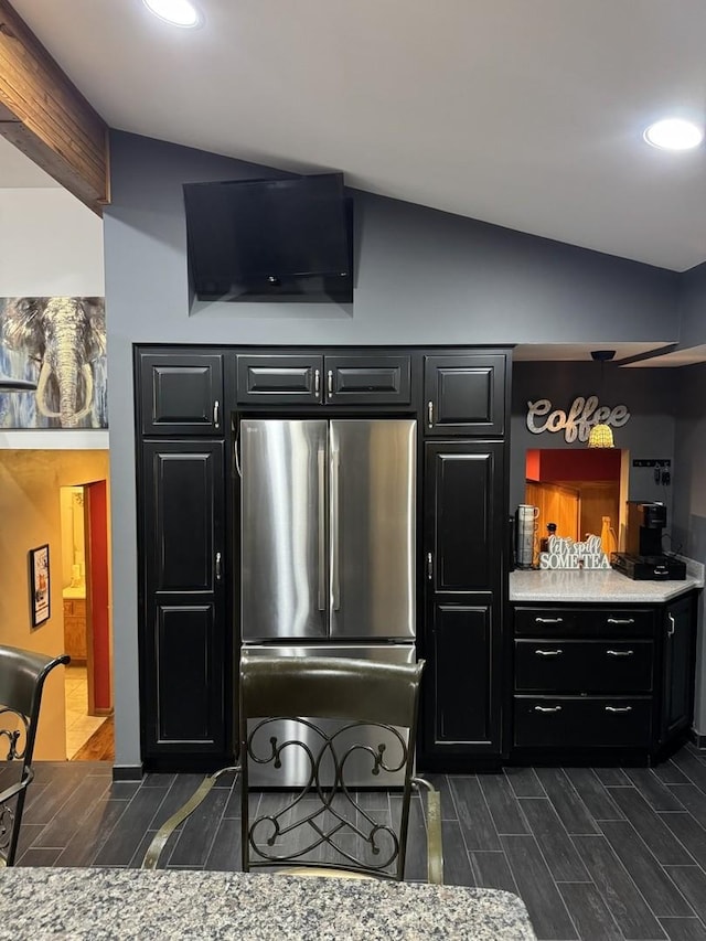 kitchen with dark cabinets, freestanding refrigerator, wood tiled floor, vaulted ceiling, and light countertops