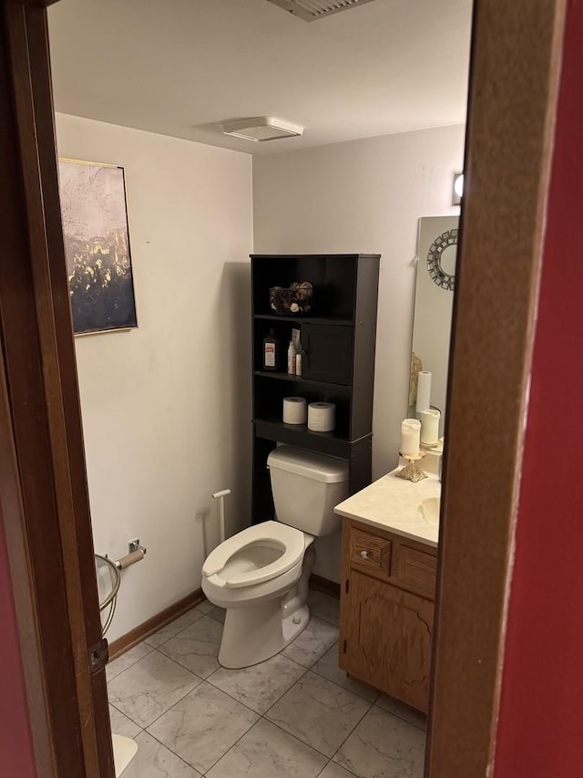 half bathroom with toilet, marble finish floor, baseboards, and vanity