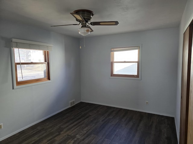 empty room with ceiling fan, a healthy amount of sunlight, and dark hardwood / wood-style flooring