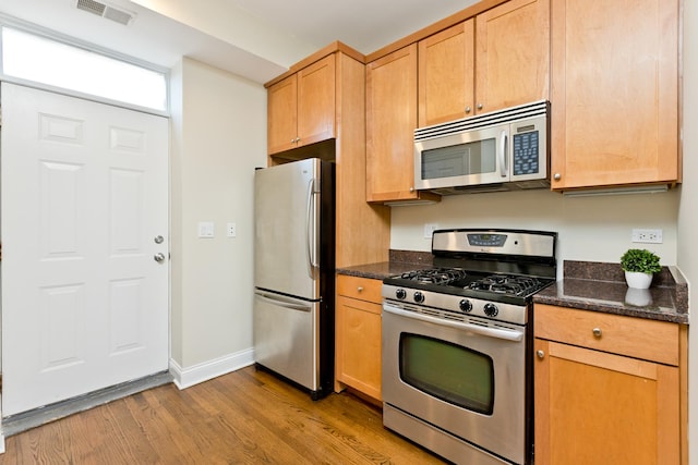 kitchen featuring appliances with stainless steel finishes, light hardwood / wood-style flooring, and dark stone countertops