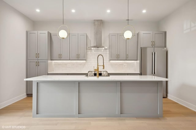 kitchen featuring gray cabinets, a center island with sink, and wall chimney range hood