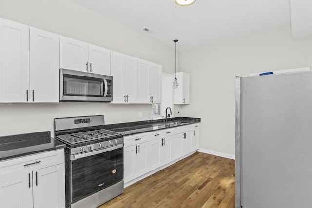 kitchen featuring pendant lighting, white cabinetry, sink, hardwood / wood-style flooring, and stainless steel appliances