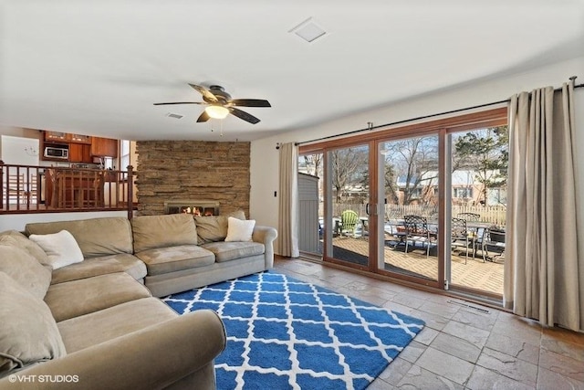 living room featuring ceiling fan, a stone fireplace, and a healthy amount of sunlight