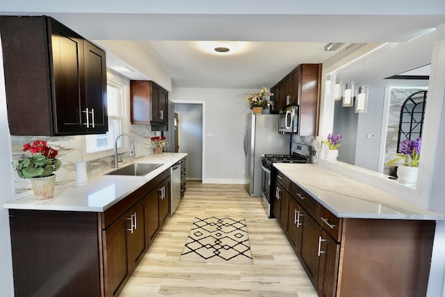 kitchen featuring sink, hanging light fixtures, light wood-type flooring, stainless steel appliances, and decorative backsplash