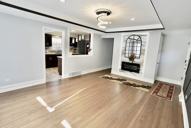 unfurnished living room with a high end fireplace, a raised ceiling, sink, and light hardwood / wood-style flooring