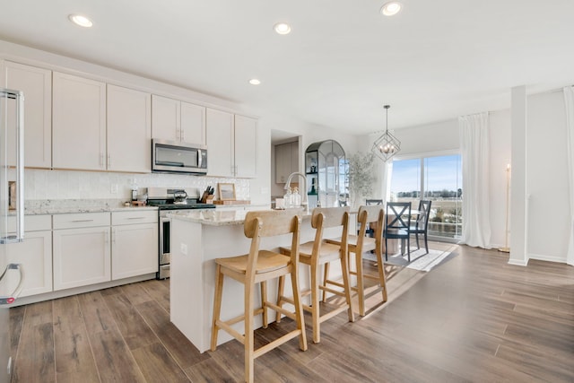 kitchen featuring white cabinetry, stainless steel appliances, an island with sink, and hanging light fixtures