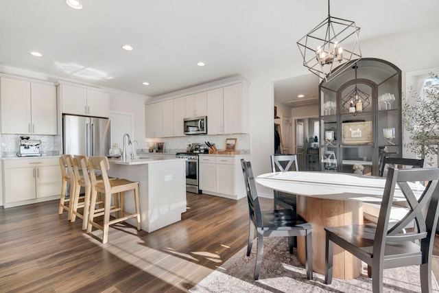 kitchen with stainless steel appliances, white cabinetry, a kitchen island with sink, and tasteful backsplash