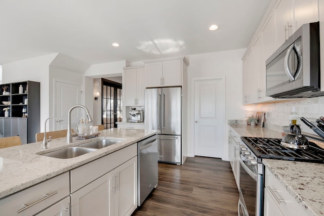 kitchen featuring sink, white cabinetry, light stone counters, stainless steel appliances, and backsplash