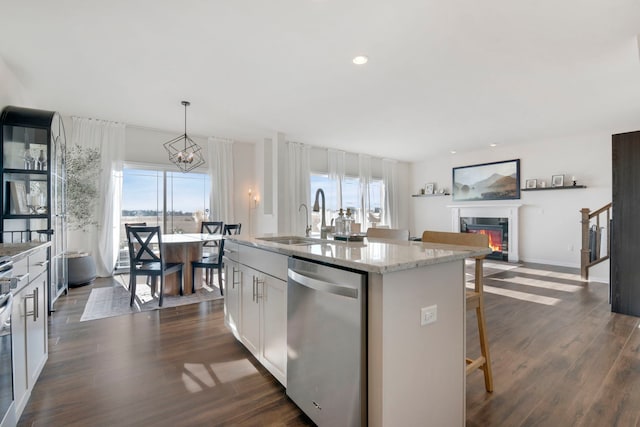 kitchen with a kitchen bar, light stone counters, decorative light fixtures, dishwasher, and a kitchen island with sink