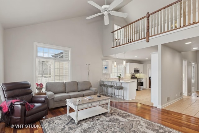 living room with high vaulted ceiling, ceiling fan, and light wood-type flooring