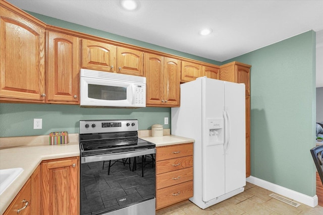 kitchen featuring visible vents, a sink, white appliances, light countertops, and baseboards