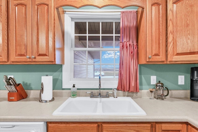 kitchen featuring brown cabinetry, dishwasher, light countertops, and a sink