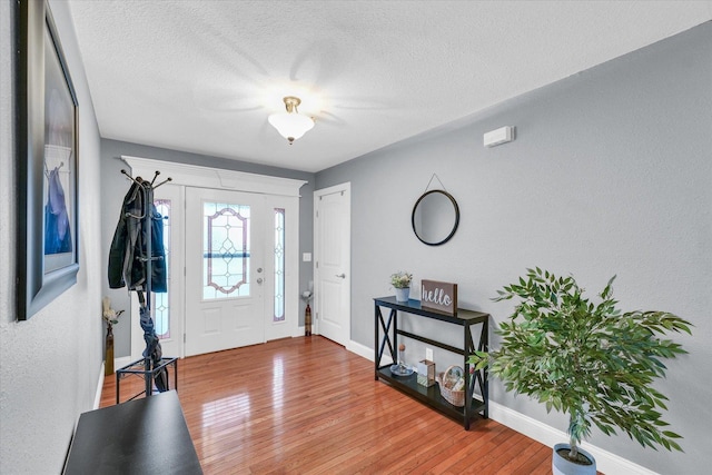 foyer entrance with a textured ceiling, baseboards, and wood-type flooring