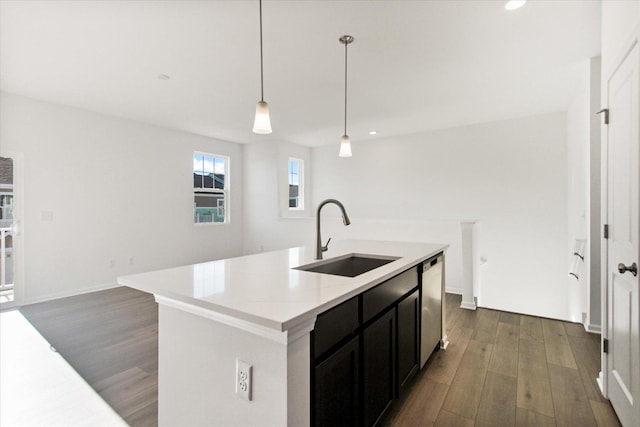 kitchen with dark wood-type flooring, sink, hanging light fixtures, stainless steel dishwasher, and a kitchen island with sink