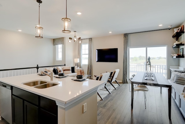 kitchen featuring sink, hanging light fixtures, light wood-type flooring, stainless steel dishwasher, and an island with sink