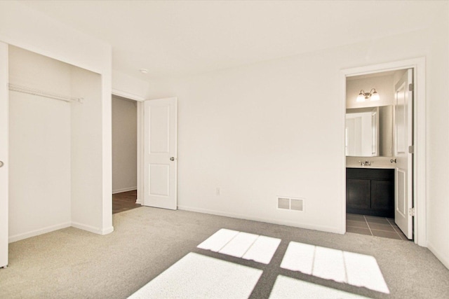 unfurnished bedroom featuring ensuite bath, sink, carpet floors, and a closet