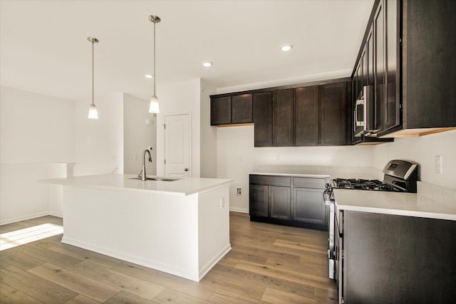 kitchen with pendant lighting, sink, stainless steel appliances, a center island with sink, and light wood-type flooring