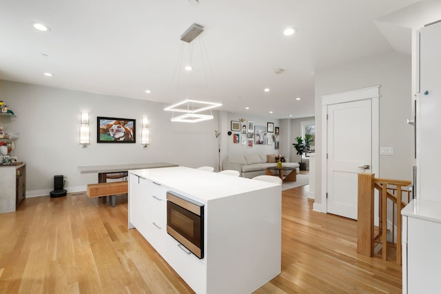 kitchen with decorative light fixtures, a center island, light wood-type flooring, stainless steel microwave, and white cabinets