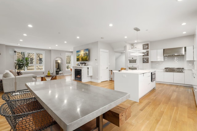 kitchen with appliances with stainless steel finishes, decorative light fixtures, white cabinets, wall chimney range hood, and a spacious island