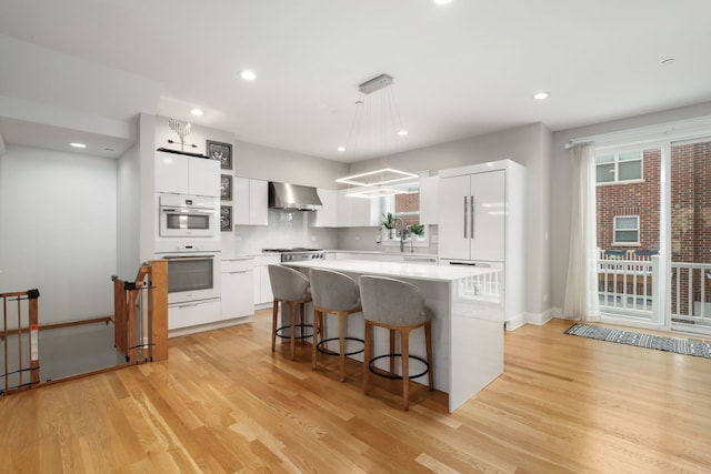 kitchen with decorative light fixtures, white cabinetry, a center island, light hardwood / wood-style floors, and wall chimney exhaust hood