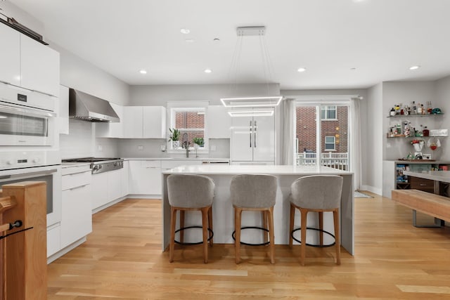 kitchen with appliances with stainless steel finishes, decorative light fixtures, white cabinetry, a center island, and wall chimney exhaust hood
