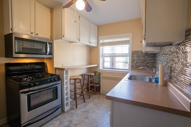 kitchen with sink, white cabinetry, tasteful backsplash, appliances with stainless steel finishes, and radiator heating unit