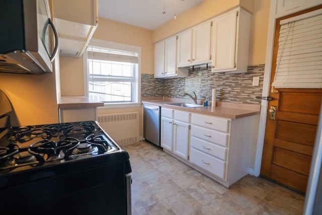 kitchen with appliances with stainless steel finishes, radiator, sink, white cabinets, and decorative backsplash