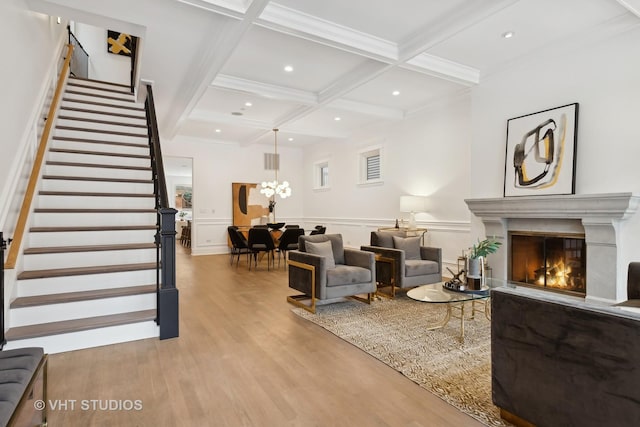 living room featuring light wood-style flooring, coffered ceiling, stairs, beam ceiling, and a glass covered fireplace