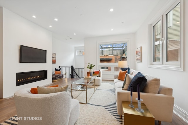 living room with recessed lighting, a glass covered fireplace, baseboards, and wood finished floors