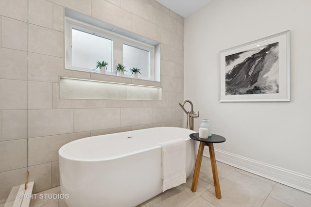 bathroom with tile patterned flooring, a freestanding tub, tile walls, and baseboards