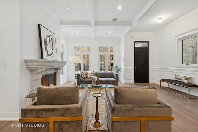 living area with a decorative wall, a fireplace, light wood-type flooring, beam ceiling, and crown molding