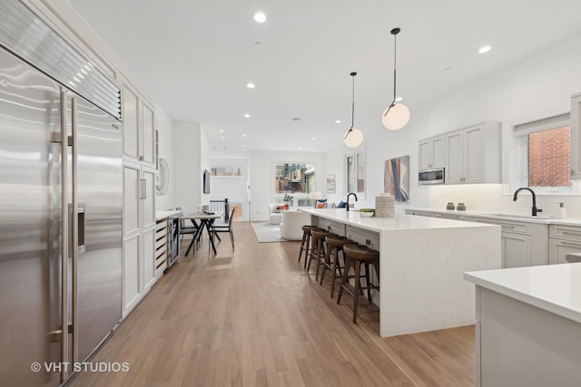 kitchen featuring built in appliances, a kitchen island, white cabinetry, light countertops, and decorative light fixtures