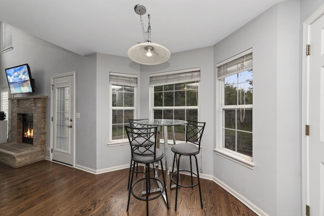 dining space with a stone fireplace and dark wood-type flooring