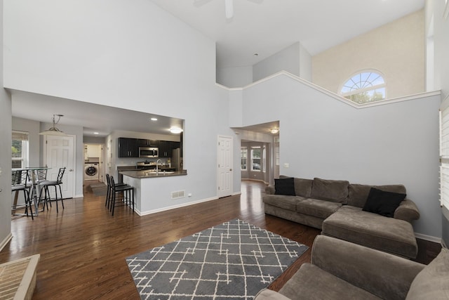 living room featuring a towering ceiling, plenty of natural light, washer / dryer, and dark wood-type flooring