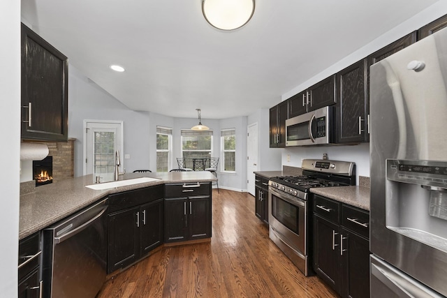 kitchen with appliances with stainless steel finishes, a fireplace, sink, hanging light fixtures, and dark wood-type flooring